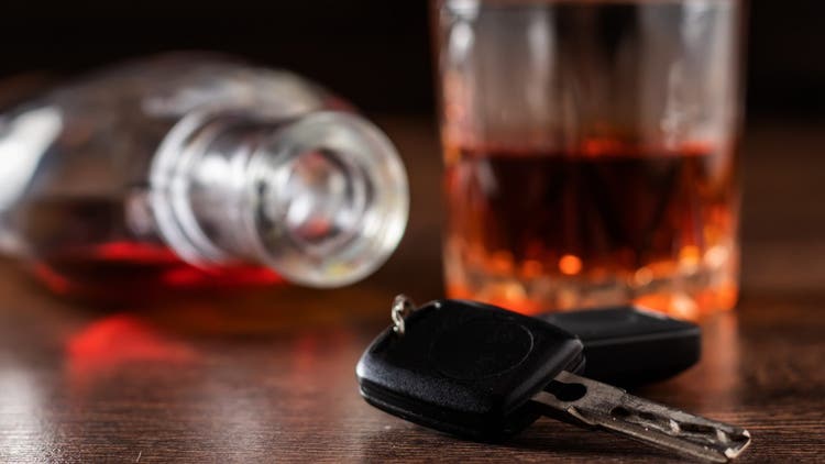 Alcoholic drink in a glass and car keys on a wooden desk. Drunk driving concept.